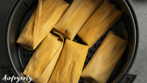 Frozen tamales arranged in a single layer inside an air fryer basket with husks still on