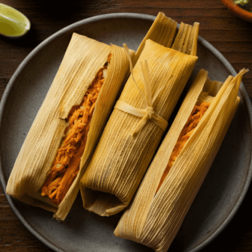 Top-down view of golden, crispy air-fried tamales served on a rustic plate with salsa and lime wedges