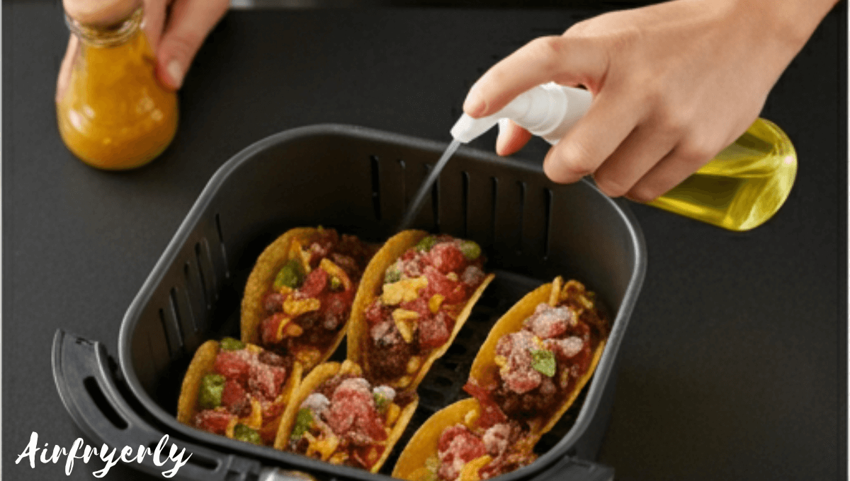 Spraying olive oil on frozen mini tacos in air fryer