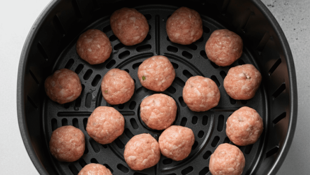 Placing uncooked sausage balls spaced out evenly inside the air fryer basket.