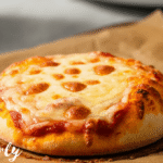 Frozen mini cheese pizza placed in air fryer basket before cooking, with even spacing and no parchment, ready for air frying.