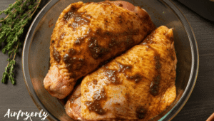 Chicken thighs coated in dark jerk marinade with visible herbs and lime slices in a mixing bowl.