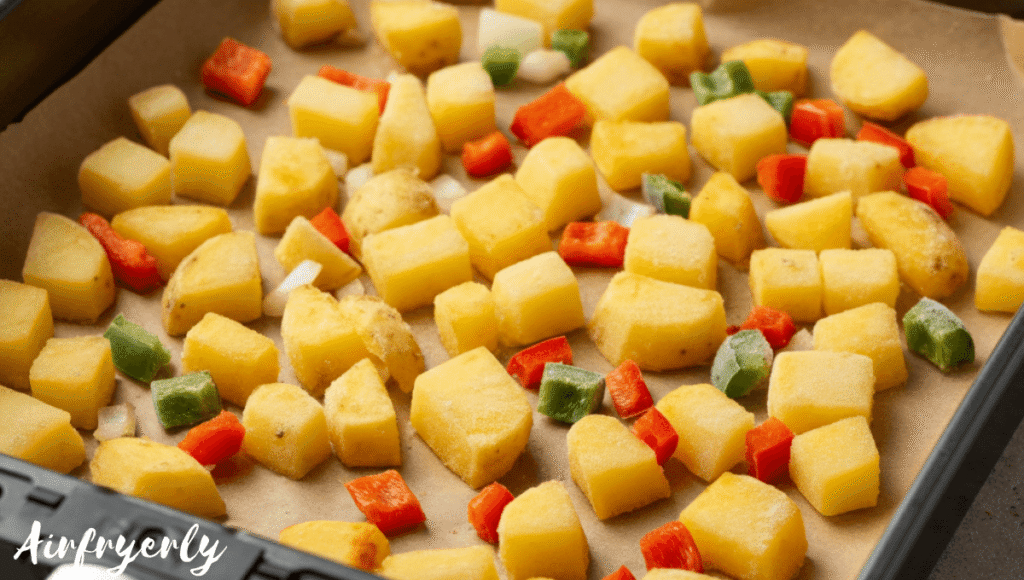 Single layer of frozen Potatoes O’Brien arranged neatly on a metal tray with colorful diced potatoes, bell peppers, and onions ready to cook. No hands or air fryer visible.
