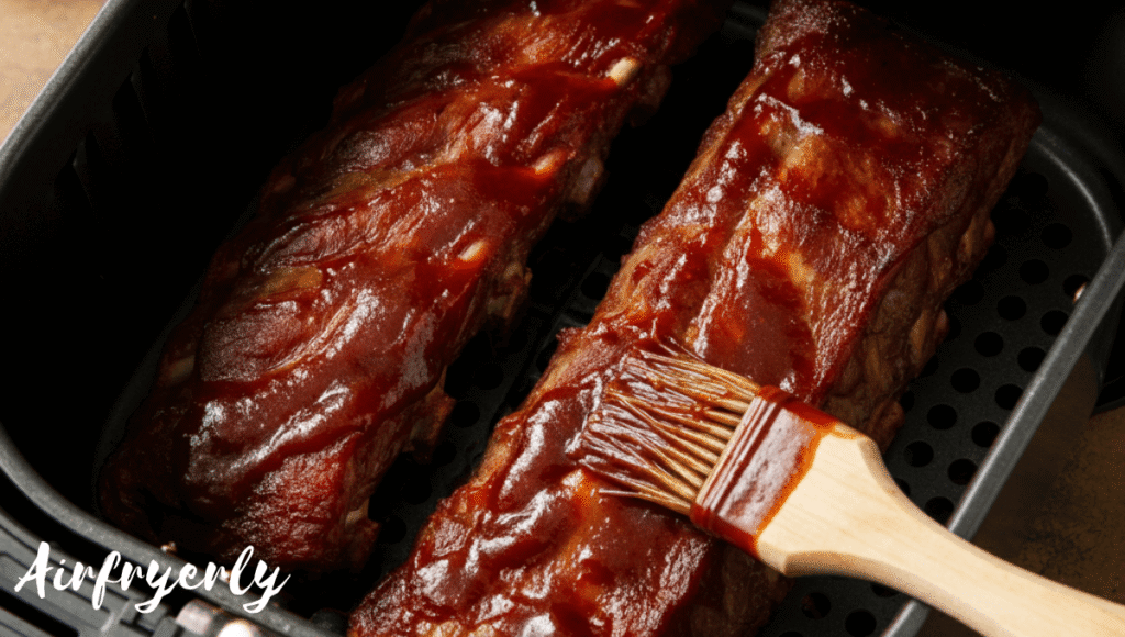 "Partially cooked air fryer beef ribs in the basket being glazed with sweet barbecue sauce for a sticky finish"