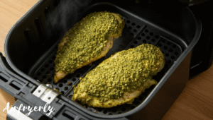 Chicken coated with pesto placed inside air fryer basket at 390°F, golden crust starting to form – air fryer pesto chicken cooking process