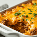 Overhead shot of a spicy air fryer ground beef casserole in a white baking dish, topped with golden melted cheese, crushed tortilla chips, and sliced jalapeños, styled with fresh cilantro on a rustic wooden table.