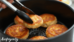 Crab cakes halfway cooked in air fryer being flipped with tongs for even crisping on both sides — How Long to Cook Frozen Crab Cakes in Air Fryer step-by-step