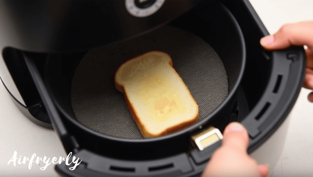 Slice of bread placed under air fryer basket to catch grease while cooking brats in air fryer for easy cleanup.