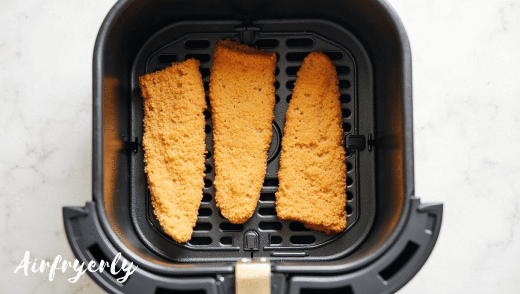 Frozen fish fillets arranged in a single layer inside the air fryer basket