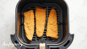 Frozen fish fillets arranged in a single layer inside the air fryer basket