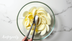 Seasoning sliced onions with oil and butter in a bowl before cooking caramelized onions in air fryer