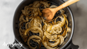 Onions cooking in air fryer basket during caramelized onions air fryer process, being stirred for even browning