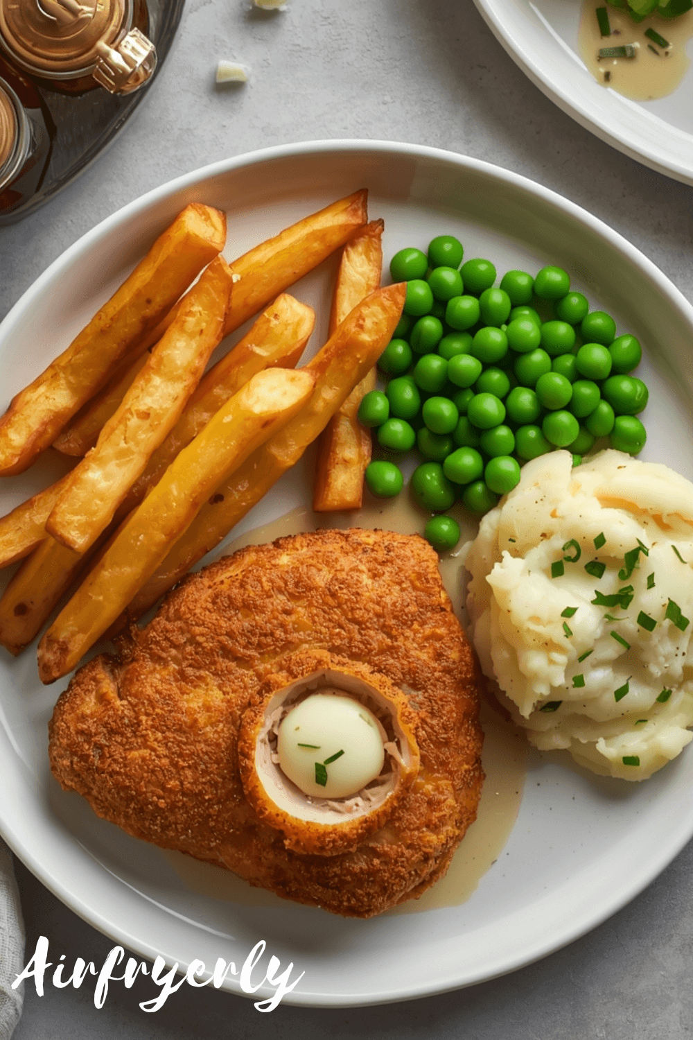 Crispy chicken kiev in air fryer served with golden fries and peas, garlic butter center visible
